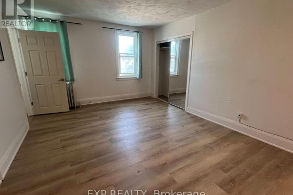 Bedroom with light laminate flooring, white walls, and a mirrored closet. A window with green curtains is visible. - 8 - 102 Greensides Avenue, Toronto