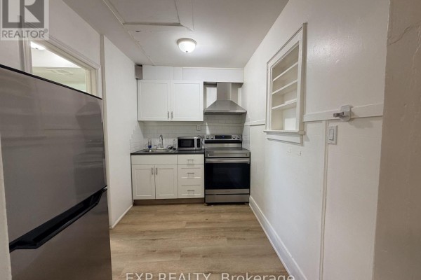 Kitchen with white cabinets, stainless steel appliances, and light laminate flooring. A window is above a cabinet. - 8 - 102 Greensides Avenue, Toronto
