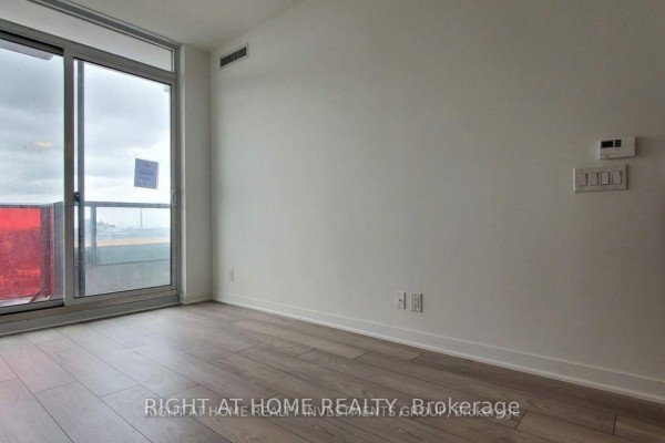Empty room with light wood flooring, white walls, and a sliding glass door. - 1408 - 120 Parliament Street, Toronto