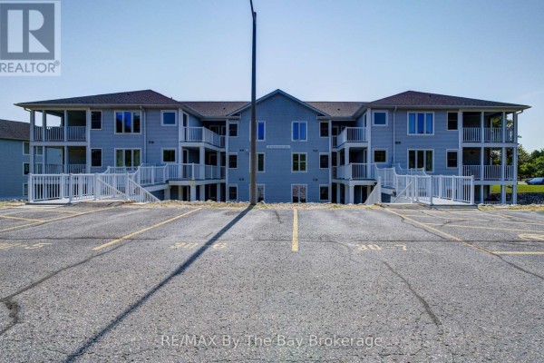 Front exterior view of light blue apartment building with balconies and parking lot with unit numbers. - 8 - 30 Mulligan Lane, Wasaga Beach