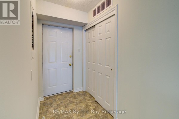 Interior view of apartment hallway with white door, closet, and textured flooring. - 8 - 30 Mulligan Lane, Wasaga Beach