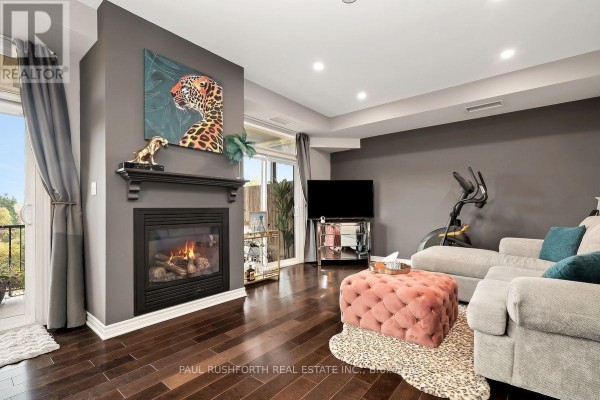 Living room with a gas fireplace, dark wood floors, grey walls, a large sectional sofa, and a sliding glass door. - 8 - 50 Prestige Circle, Ottawa
