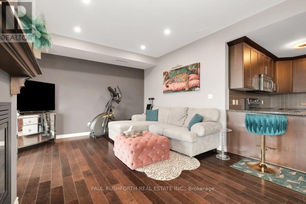 Open-concept living space with a grey sectional sofa, gas fireplace, dark wood floors, and a partial view of the kitchen. - 8 - 50 Prestige Circle, Ottawa