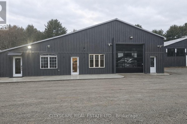 Dark grey commercial building exterior with windows and a glass roll-up garage door. - 8 - 8021 35 Highway, Kawartha Lakes
