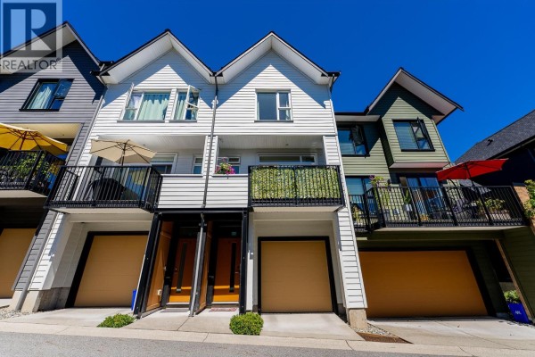 Exterior view of a row of townhouses with white siding, balconies, and garage doors. - 8 1228 Hudson Street, Coquitlam