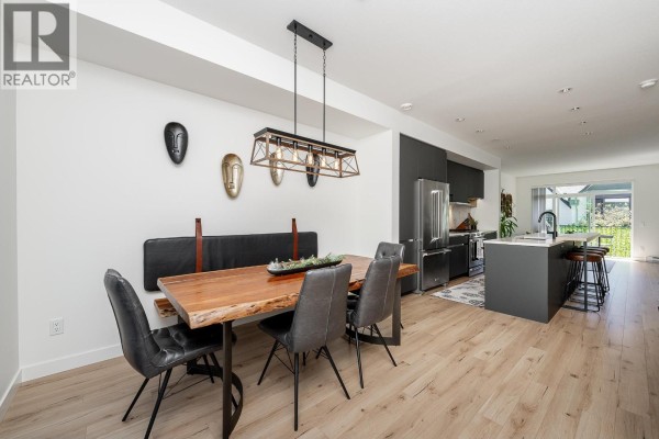 Open-concept dining room and kitchen area with a live-edge table, island with bar stools, and stainless steel appliances. - 8 1228 Hudson Street, Coquitlam