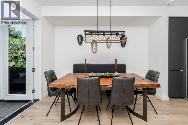 Dining area with a live-edge wood table, grey upholstered chairs, and a view of the kitchen and backyard access. - 8 1228 Hudson Street, Coquitlam