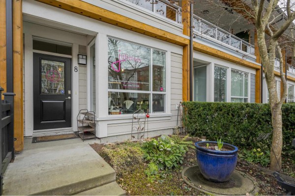 Front entrance of a townhouse unit featuring a black door, large window, and garden. - 8 23230 Billy Brown Road, Langley