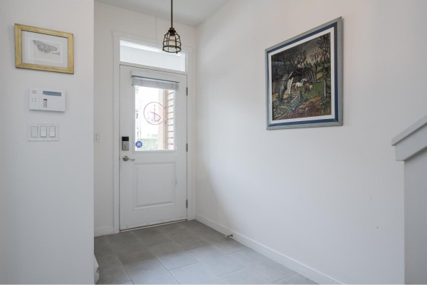 Interior view of a townhouse entrance hall with a white door, tiled floor, and artwork. - 8 23230 Billy Brown Road, Langley