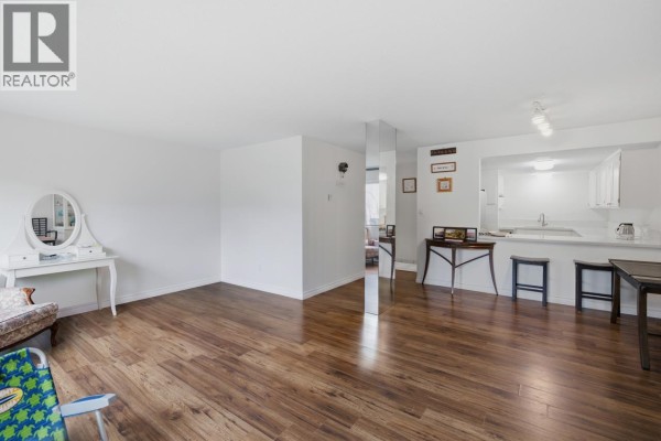 Living room and kitchen area with wood floors, white walls, and a breakfast bar. - 8 7363 Montecito Drive, Burnaby