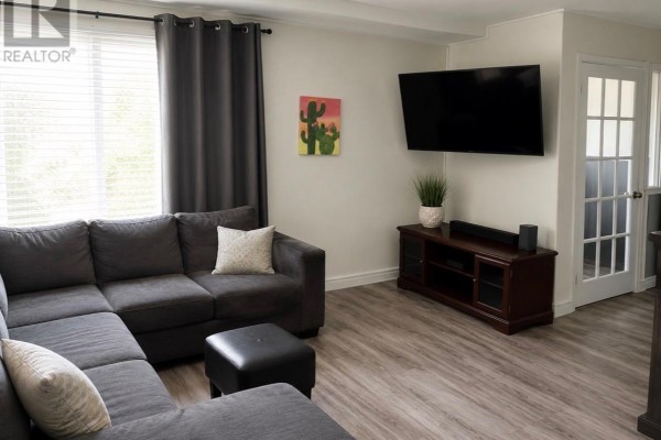 Living room with a large sectional sofa, television mounted on the wall, and a dark wood media console. - 8 Banting Avenue, Wabush