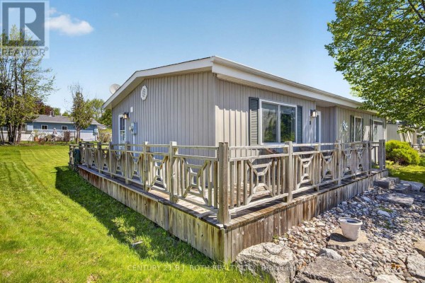 Corner view of the home showing the wooden deck, railing, and surrounding grass. - 8 Belle Isle Arm, Innisfil