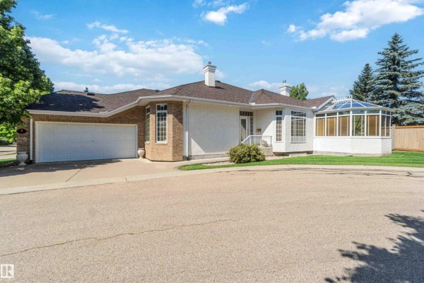 View of the duplex exterior from the curved driveway with green lawn and trees. - 8 Butterworth Pt Nw, Edmonton