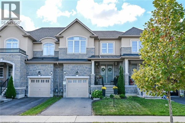 Front view of a townhouse complex with stone and beige accents, well-maintained landscaping, and a clear sky. - 8 Callon Drive, Ancaster