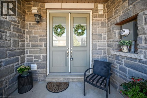 Detailed view of a townhouse's grey double front doors, surrounded by stone exterior walls and a small porch chair. - 8 Callon Drive, Ancaster