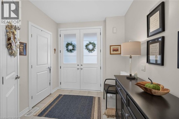 Interior foyer of a townhouse with tile flooring, double glass doors, a console table, and framed artwork. - 8 Callon Drive, Ancaster