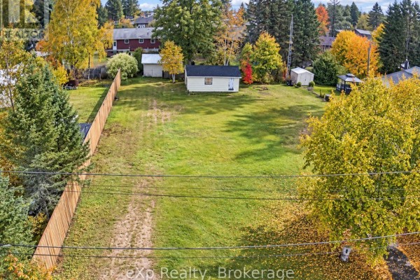 Aerial view of a cleared lot with grass, a small white building, and surrounding trees. - 8 Cedar Court, South River