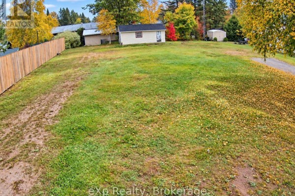 View across a grassy lot with fallen leaves and a worn asphalt path. - 8 Cedar Court, South River