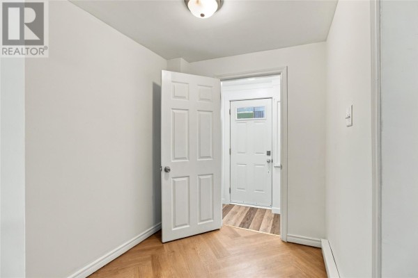 Interior view of a small room with light green walls, herringbone wood flooring, and an open white door. - 8 Charlton Street, St  John S