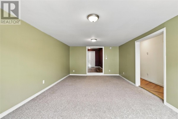 Spacious living area with light green walls, beige carpet, and three doorways leading to other interior spaces. - 8 Charlton Street, St  John S