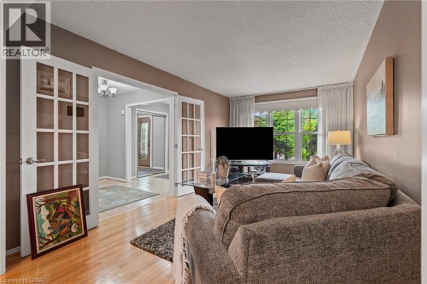Living room with a grey sofa and a view of the entryway through French doors. - 8 Cochrane Avenue, Brampton