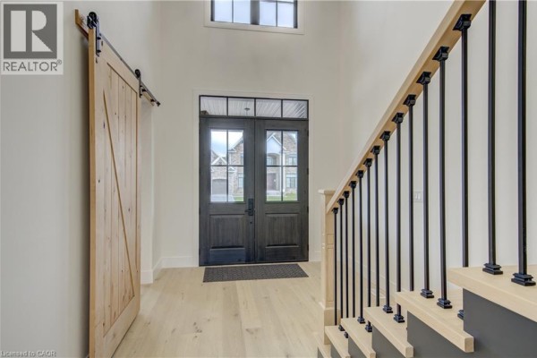 Entrance hall with light wood floors, double front doors, and a rustic wood barn door. - 8 Edgeview Crescent, Komoka