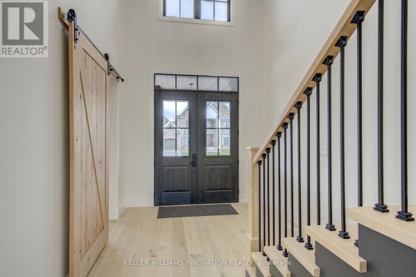 Spacious foyer with double front doors, a wooden barn door, and a staircase with black spindles. - 8 Edgeview Crescent W, Middlesex Centre