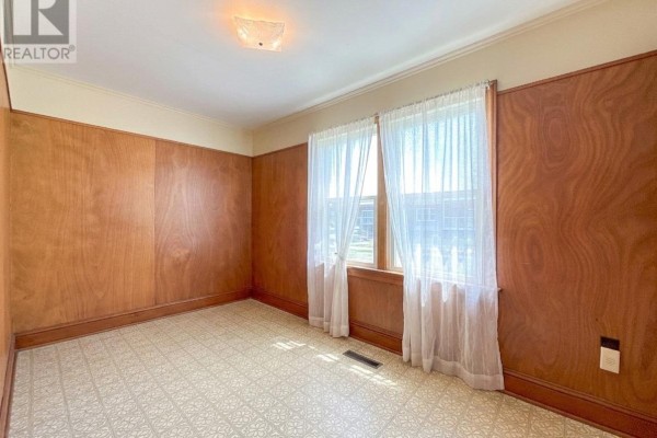 Interior room with wood-paneled walls, beige patterned floor, and sheer curtains covering windows. - 8 Falconwood Drive, Charlottetown