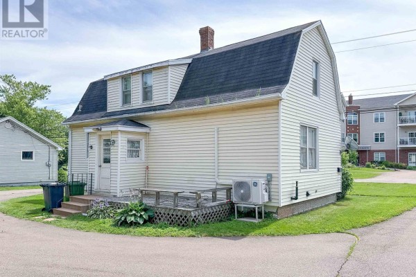 Rear exterior of a cream-colored house with a wooden deck, air conditioning unit, and surrounding green lawn. - 8 Falconwood Drive, Charlottetown