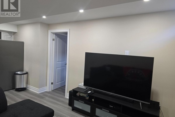 Finished basement with a doorway, large television on a stand, and a stainless steel trash bin. - 8 Hassard-short Lane, Ajax