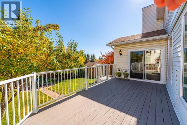 A wide composite deck with white railings overlooks a green backyard and mature trees. - 8 Hawkdale Close Nw, Calgary
