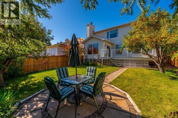 A circular stone patio with a glass-top table and four chairs is set in a grassy backyard. - 8 Hawkdale Close Nw, Calgary