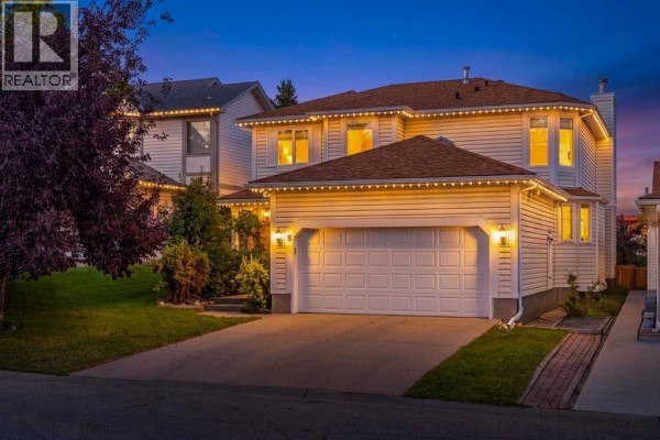 The front of a two-story house with a double garage, illuminated by outdoor lights at twilight. - 8 Hawkdale Close Nw, Calgary