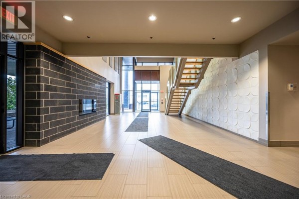 Building lobby with dark brick accent wall, fireplace, and entrance doors. - 8 Hickory Street W Unit# 404, Waterloo
