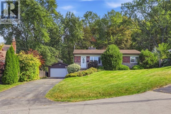 Front exterior of a brick house with a sloped green lawn and mature trees. - 8 Hill Place, Stoney Creek
