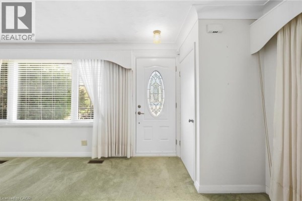 Interior view of a living room with light green carpet, a large window, and a white front door. - 8 Hill Place, Stoney Creek
