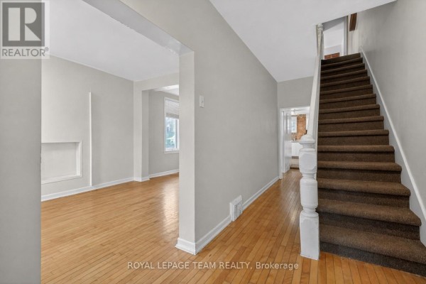 Hallway with hardwood floors, staircase with brown carpet, and doors to rooms. - 8 Lewis Street, Ottawa