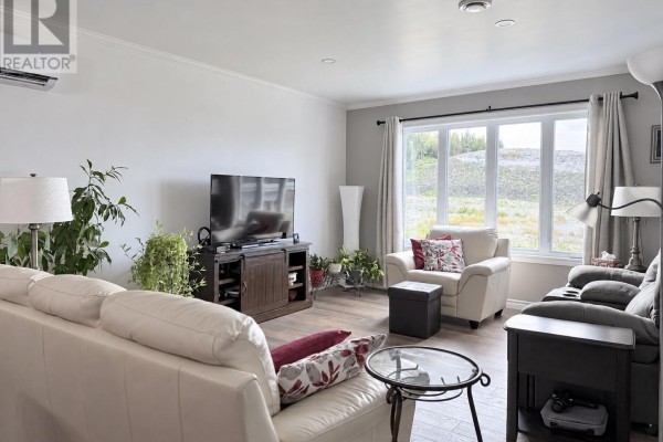 Living room with white sectional sofa, armchair, TV stand, and large window with curtains. - 8 Parkway Heights, Corner Brook