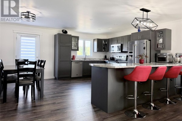 Kitchen with dark gray cabinets, granite countertops, island with red stools, and dining table. - 8 Parkway Heights, Corner Brook