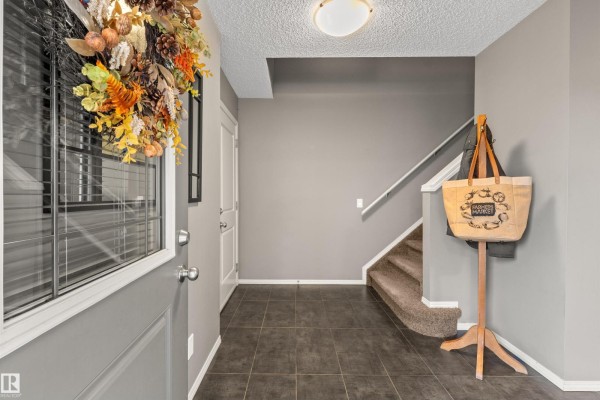 Foyer with grey tiled floor, beige carpeted stairs, and a coat rack. - 8 Royal St, St  Albert