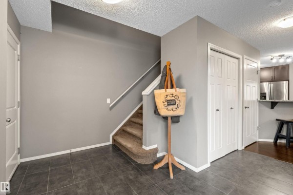 Entranceway showing grey walls, tiled floor, carpeted stairs, and closet doors. - 8 Royal St, St  Albert