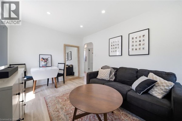 Living room with a grey sofa, coffee table, white dresser, and a black door. - 8 Russell Street, Brantford