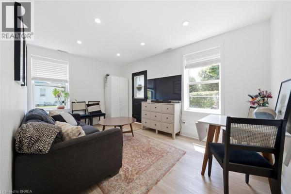 Living room with a sofa, rug, dresser, and a large mirror reflecting the doorway. - 8 Russell Street, Brantford