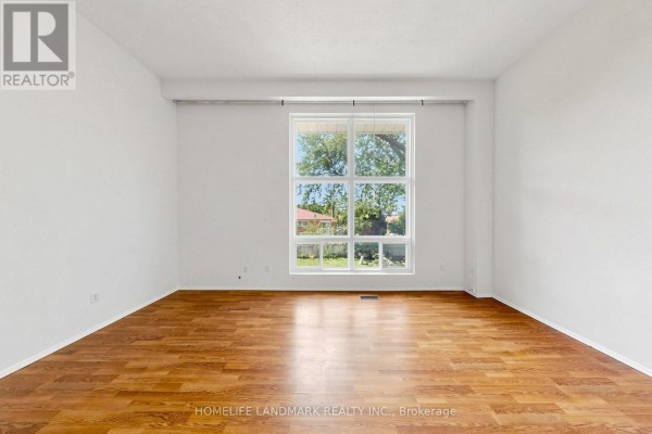 Empty room with light walls, hardwood floors, and a large window overlooking a backyard. - 8 Rusty Crest Way, Toronto