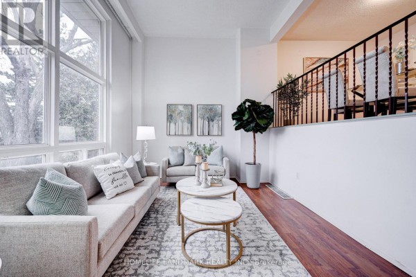 Living room with light grey sofas, marble coffee tables, hardwood floors, a large window, and a staircase. - 8 Rusty Crest Way, Toronto