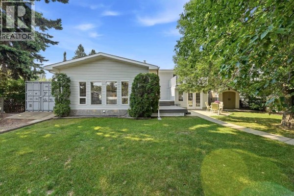Wide view of the house exterior from the backyard with grass and trees. - 8 Sydney Close, Red Deer