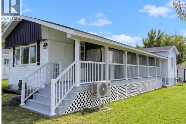 Side exterior view of the bungalow with a large covered wrap-around deck featuring white railings. - 8 Tait Crescent, Moncton