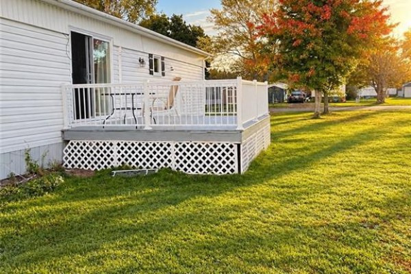 Rear exterior of the bungalow showing a white deck with white railings and lattice skirting. - 8 Tait Crescent, Moncton