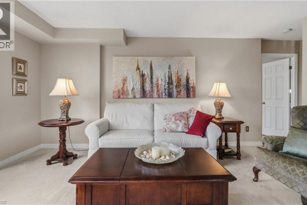 Living room with beige carpet, white sofa, and wooden side tables with lamps. - 8 Village Green Boulevard Unit# 510, Hamilton