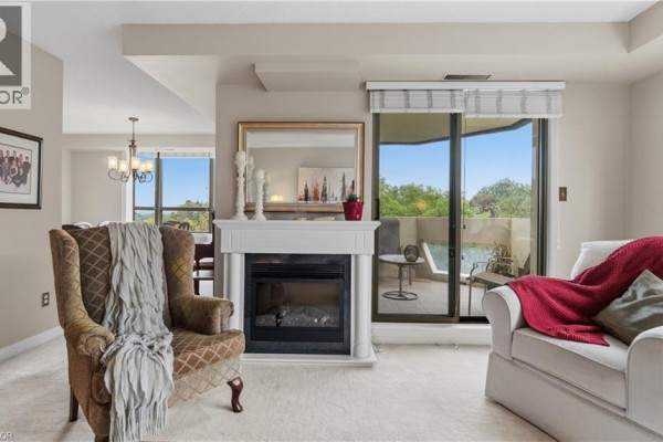 Living room with a fireplace, sofa, armchair, and glass doors leading to a balcony. - 8 Village Green Boulevard Unit# 510, Hamilton